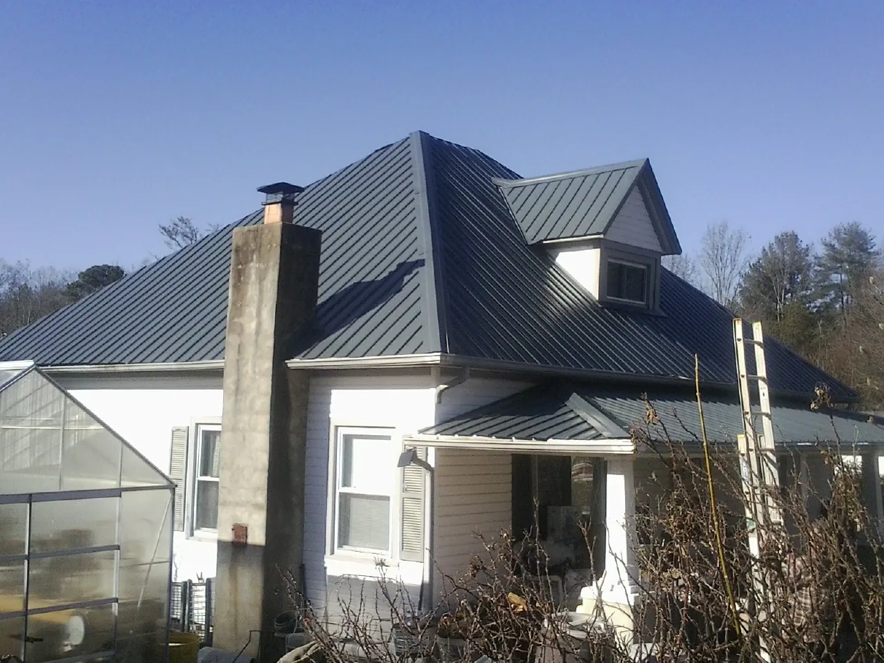 Dark blue standing seam metal roof on a white farmhouse with dormer — Slate & Tile Roof Repair by Roofing Brothers in Center Harbor