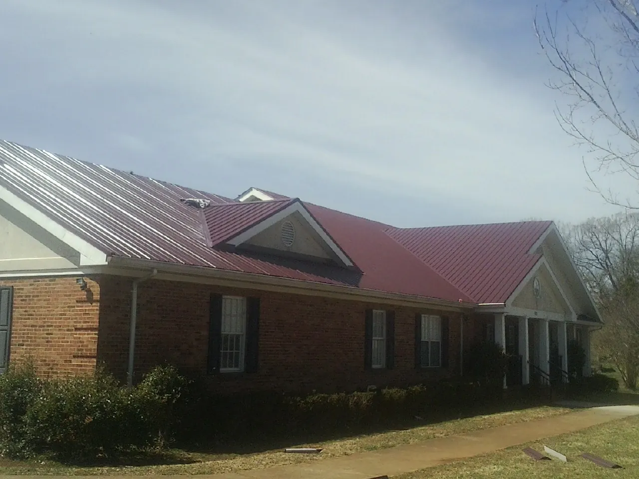 Red metal roof with gabled entries on a long brick building, from a Hail Damage Roof Repair job in Center Harbor