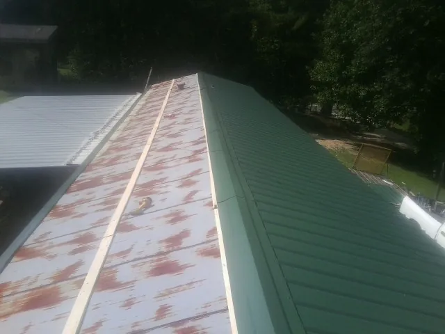 Old rusted panels beside newly installed green metal roofing — Wind Damage Roof Repair by Roofing Brothers in Center Harbor