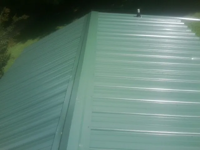 New green metal panels meeting at the ridge of a roof — Flat Roof Repair work by our crew in Center Harbor