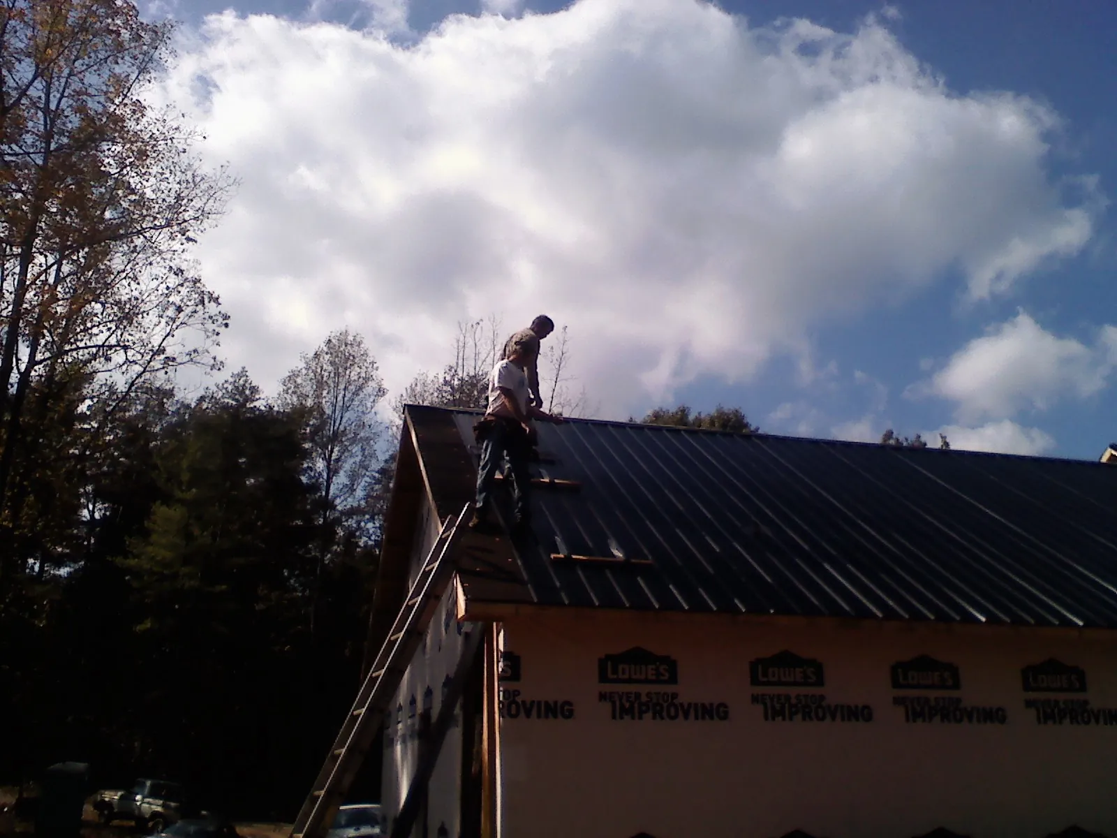 Roofer fastening dark metal panels high against a cloudy sky, from a Roof Inspection job in Center Harbor