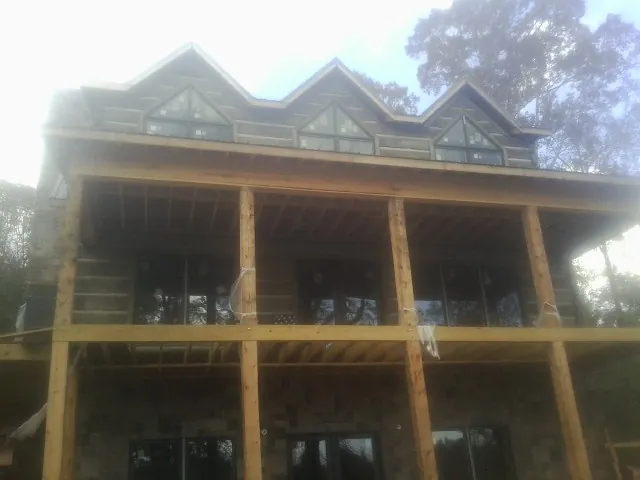 Dormers and porch framing on a large log home under construction — Roof Coating work by our crew in Center Harbor
