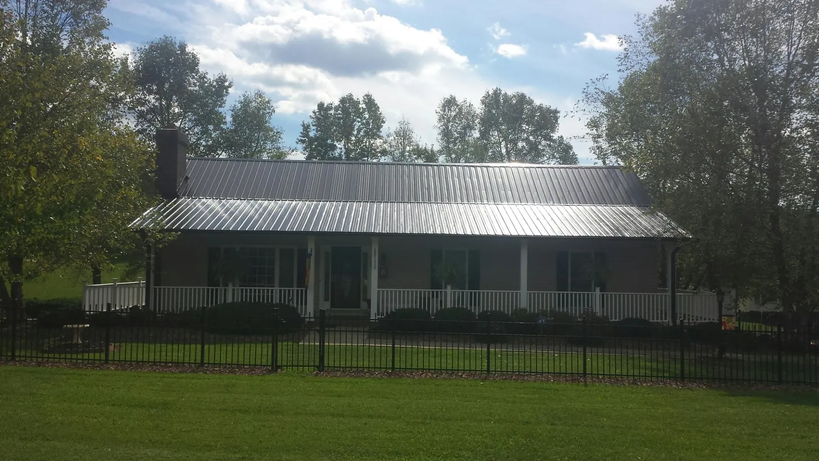 Gray metal roof on a brick ranch with a full width front porch — Gutter Guard Installation work by our crew in Center Harbor