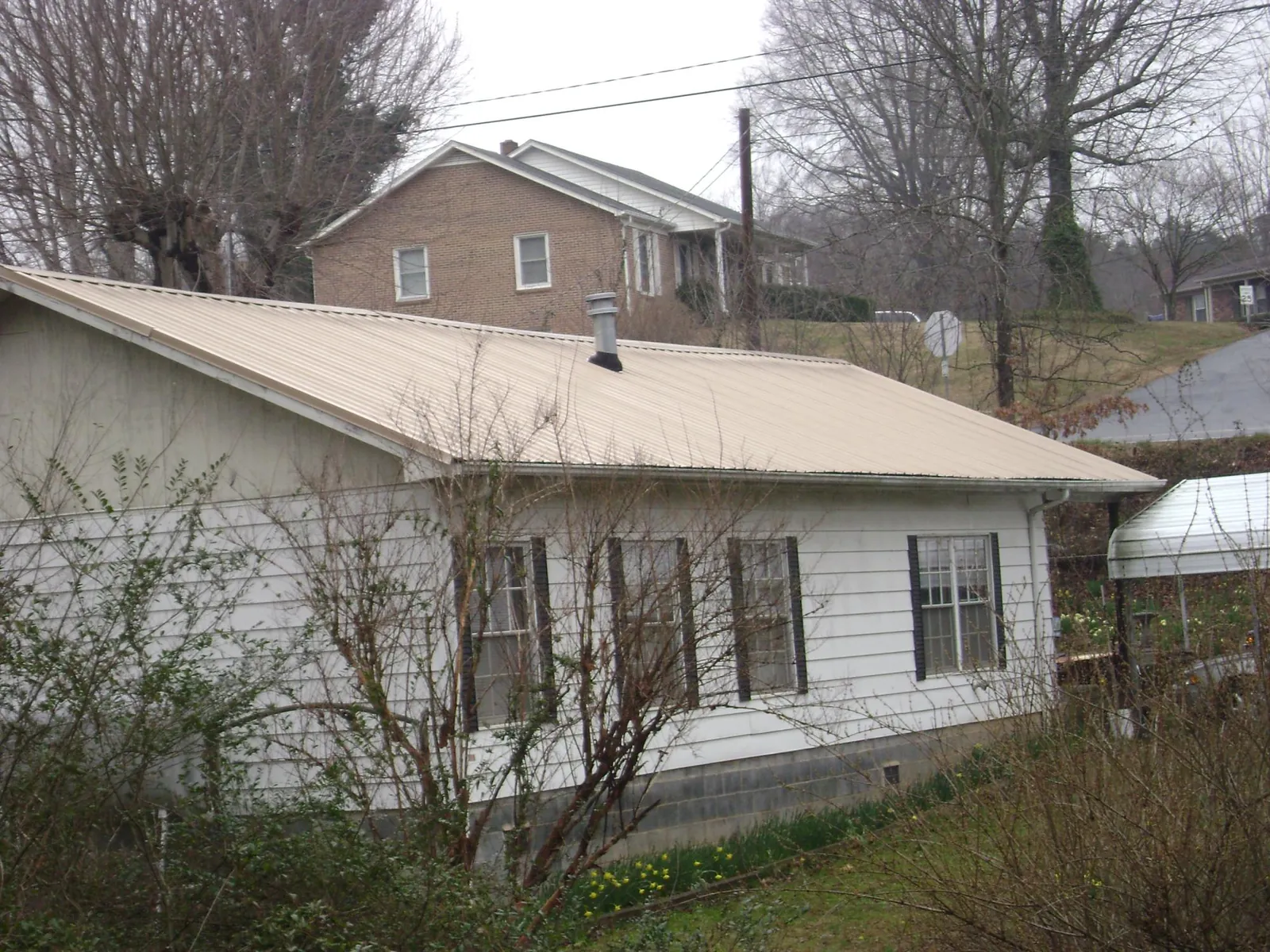 Tan metal roof on a white sided house set into a hillside — Commercial Roofing by Roofing Brothers in Center Harbor