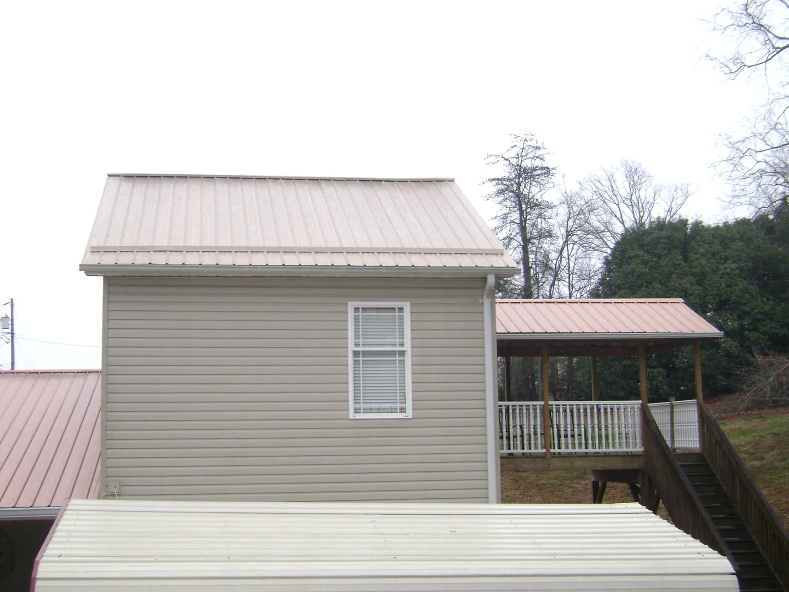 Tan metal roofs on a two story addition and attached porch, from a Roof Replacement job in Center Harbor