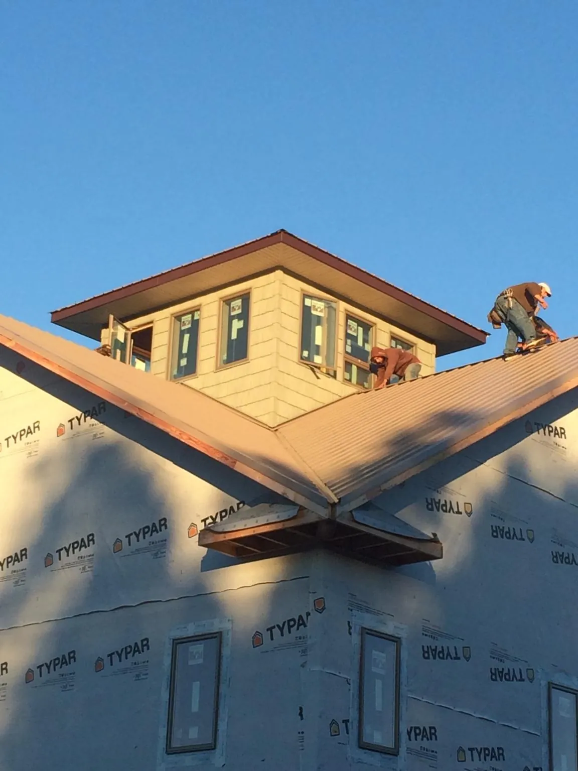 Roofers working around a rooftop cupola on a new metal roof at sunset — Roof Waterproofing in Center Harbor by Roofing Brothers